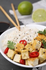 Bowl of rice with fried tofu, chili pepper and parsley on grey wooden table, closeup