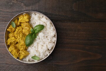 Delicious rice and chicken with curry sauce on wooden table, top view. Space for text