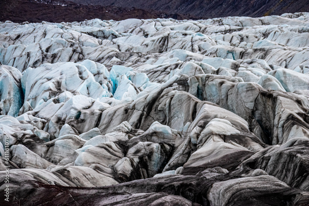 Wall mural Glacier erosions in Iceland with black volcanic dust on the ice on a cold day in spring, climate change