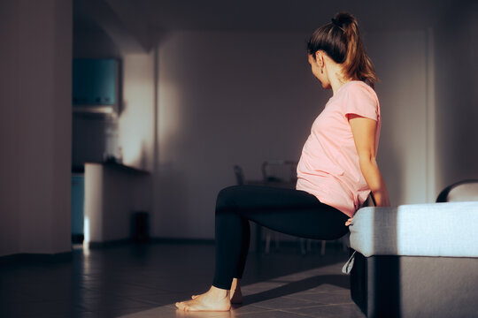 Woman Exercising at Home Using a Sofa as improvised Equipment. Young pregnant girl trying to exercise in her Livingroom 
