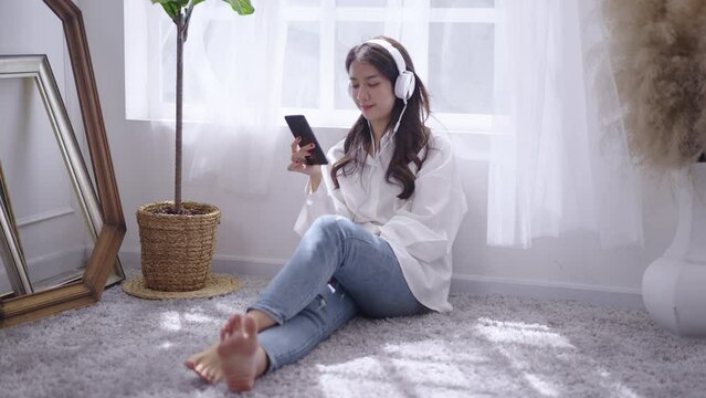 Young Asian woman listening to music at home from smartphone