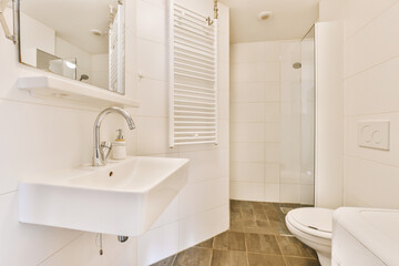 Fototapeta na wymiar a white bathroom with wood flooring and tile on the walls, along with a walk - in shower stall
