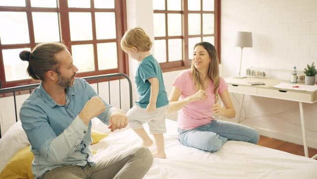 Happy Caucasian father and mother playing with little baby son on the bed in bedroom. Parents and child boy kid enjoy and fun indoors activity lifestyle together at home. Family relationship concept.