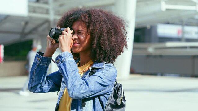 Attractive african american black teenager girl standing in the city, using a vintage digital camera taking photographs. Photography student and tourism lifestyle