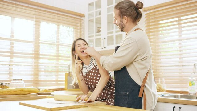 Happy Caucasian couple kneading dough on island counter with playing together in the kitchen at home. Husband and wife enjoy and fun indoors activity cooking together. Family relationship concept.