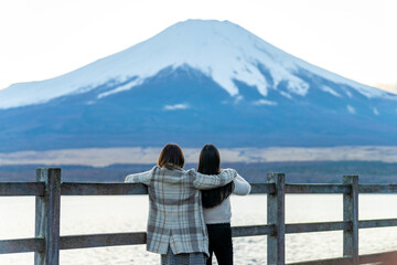Happy Asian woman travel Japan on autumn holiday vacation. Attractive girl friends enjoy and fun outdoor lifestyle travel the lake around Mt Fuji covered in snow and looking beautiful nature together.