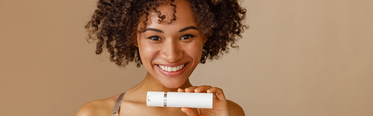 Young woman holding bottle with beauty product in studio