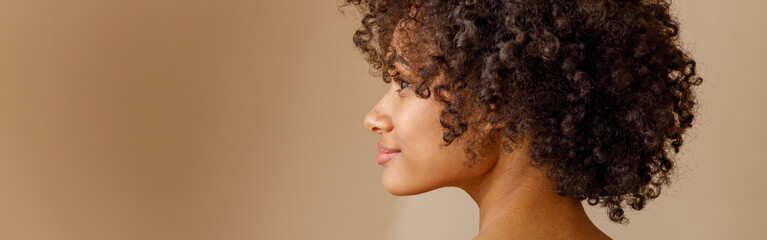 Charming multiracial woman posing against beige wall