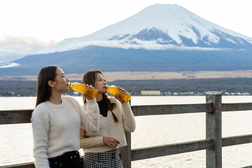 Happy Asian woman friends travel nature in Japan on autumn holiday vacation. Attractive girl enjoy outdoor lifestyle drinking tea together during travel Kawaguchi lake and Mount Fuji covered in snow.