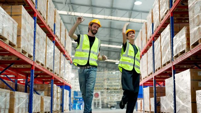 Young warehouse workers in uniform and helmet protective having fun and dancing in factory storehouse. Manual workers wearing vest and safety helmet having fun and happy relaxing in warehouse