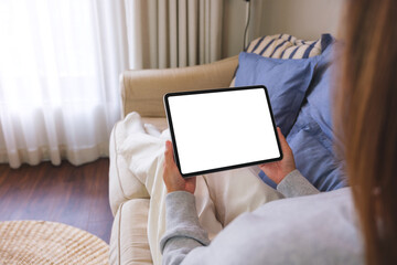 Mockup image of a woman holding digital tablet with blank desktop screen while lying on a sofa at home