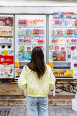Happy Asian woman choosing and buying drinks on snack and beverage vending machine while shopping at shibuya, Tokyo, Japan. Attractive girl enjoy and fun outdoor travel city street on autumn vacation.