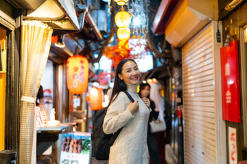 Asian woman shopping at street market and looking for izakaya restaurant at Shinjuku district, Tokyo city, Japan. Attractive girl enjoy and fun outdoor lifestyle travel Japan on holiday vacation.