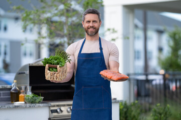 man smiling with salmon in apron. photo of barbecue man with salmon fish.
