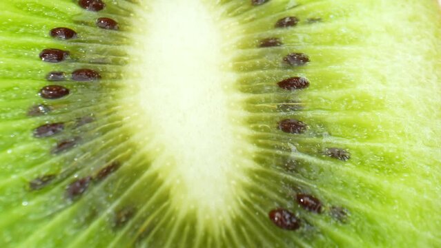 Macro video showcases the intricate details of a halved kiwi fruit: succulent green flesh, a plethora of tiny black seeds, and a burst of tangy sweetness. Food and health concept. Kiwi background
