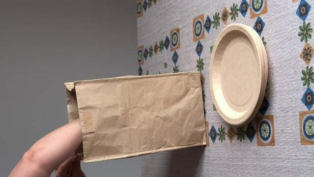 hand taking paper, cardboard and wooden cutlery and plates from a paper bag and putting them on the table
