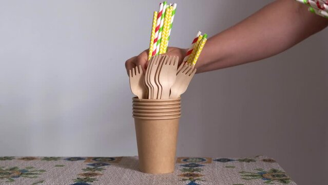 woman's hand catches or takes a disposable paper straw between gold biodegradable cutlery
