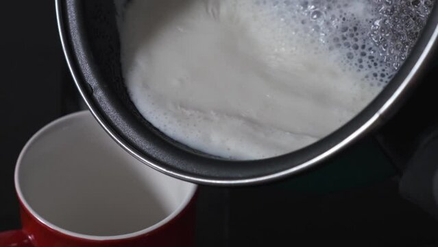 pouring hot milk from a saucepan into a mug in the kitchen
