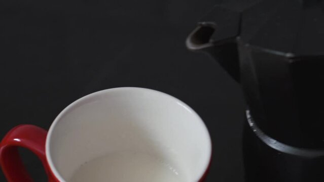 serving coffee from freshly brewed moka pot in red cup with milk
