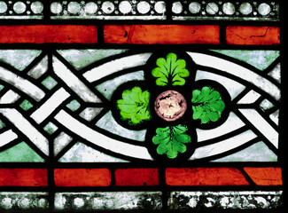 Close up of stained glass panel in a church showing celtic knot work, four green leaves and a red border - Powered by Adobe