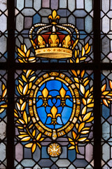 Detail of stained glass panel with a crown, gold leaves, three gold fleur de lys on blue background in St. Denis Basilica, Paris France