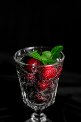 ripe red berries in a glass with a sparkling drink with bubbles and green mint leaves. summer drinks. non-alcoholic cocktail
