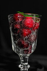 ripe red berries in a glass with a sparkling drink with bubbles and green mint leaves. summer drinks. non-alcoholic cocktail