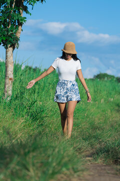 girl walking in a rice field path with a hat