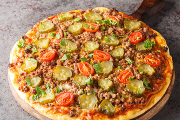Cheeseburger Pizza is topped with a creamy burger sauce, ground beef, cheese and pickles closeup on the wooden board on the table. Horizontal