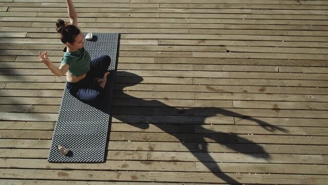 a woman doing yoga working with her shadow sitting on a wooden deck