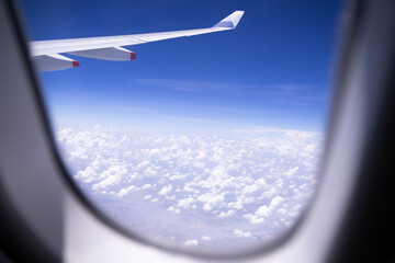 Naklejka na ściany i meble Airplane wings flying above the clouds on bright blue sky airplane window view