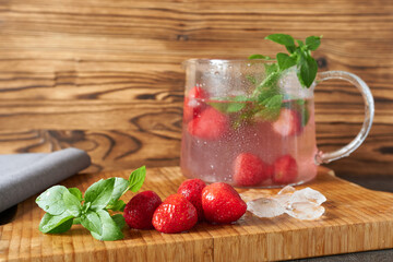 Refreshing summer drink with strawberries, mint and ice on wooden background