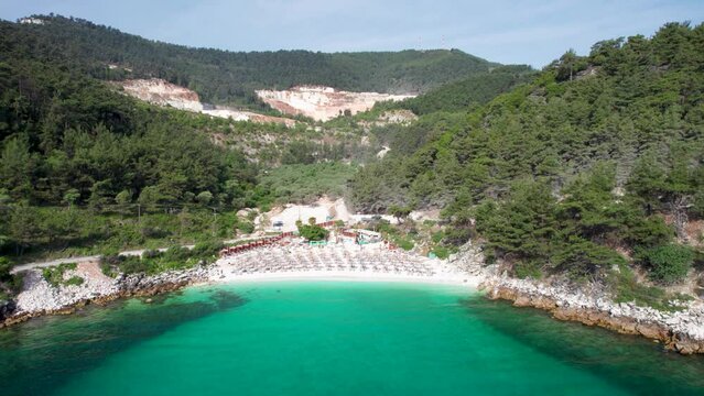 Cinematic Drone View Of Marble Beach, Clear Water, White Pebbles And Lush Green Vegetation, Empty Beach, Umbrellas, Thassos Island, Greece, Mediterranean Sea, Europe