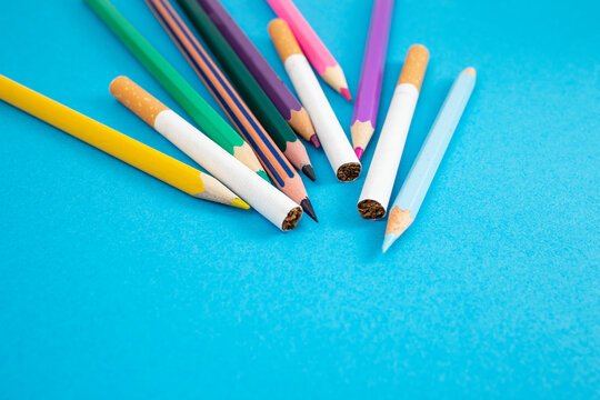 cigarettes between colored crayons on blue paper backdrop