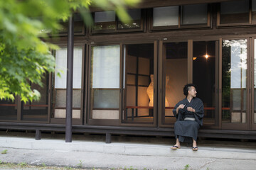 日本の田舎や旅館に旅行にきて縁側でお酒を飲む浴衣の日本人男性　広角