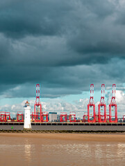 Tall red cranes on port of Liverpool docks and Perch rock lighthouse with stormy clouds