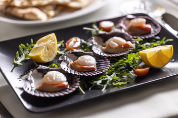 St Jacob scallops served on a dark plate with wedges of lemon and rocket salad