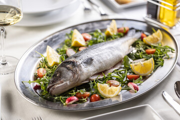 Sea bass raw fish staged on a silver tray on green, red and yellow coloured salad