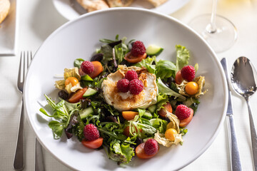 Top view of a mixed salad with grilled goat cheese, raspberries and balsamic vinegar