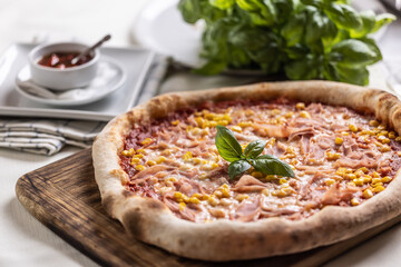 Italian pizza with corn and basil leaves served on a wooden board
