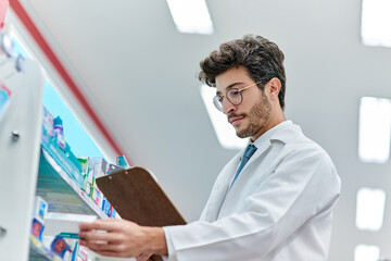 Pharmacist, clipboard and a man in pharmacy or working in a store for retail career. Male person in pharmaceutical or medical industry for service, healthcare and reading to check inventory on shelf
