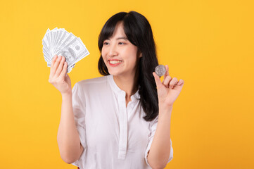 Portrait beautiful young asian woman enterpriser happy smile wearing white shirt and red plants holding cash dollar money and crypto digital currency isolation on yellow background. Wealth concept.