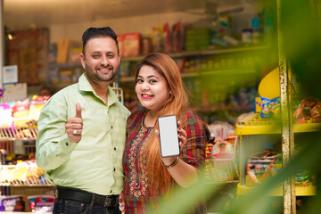 Indian couple showing smartphone screen at grocery shop.