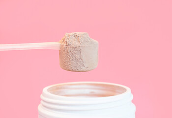 Chocolate protein powder in scoop and plastic jar on pink background. - obrazy, fototapety, plakaty