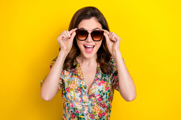 Photo of astonished positive girl open mouth hands touch sunglass isolated on yellow color...