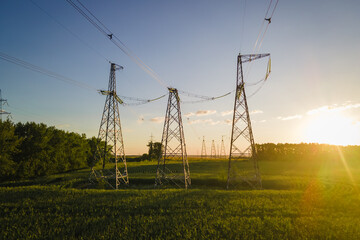 High voltage electric power tower in a green field at sunset, agricultural landscape