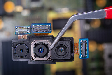 Close-up of a smartphone's triple camera held with tweezers