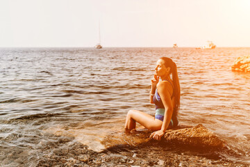Woman travel summer sea. A happy tourist in a blue bikini enjoying the scenic view of the sea and volcanic mountains while taking pictures to capture the memories of her travel adventure.