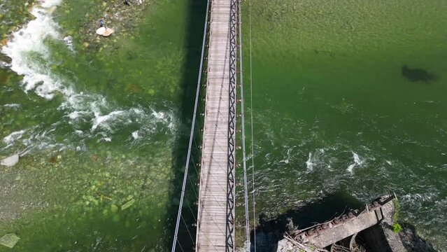 Drone flight over a wooden Tibetan suspended bridge that joins the river banks - view from the drone in Alagna Val Sesia Piedmont Alps mountains - travel concept journey in adventure natural trip 