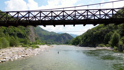 Drone flight over a wooden Tibetan suspended bridge that joins the river banks - view from the...